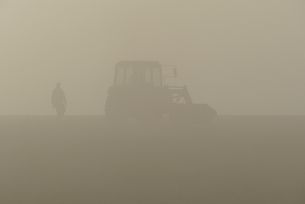 Traktor und Bauer auf Feld im Nebel